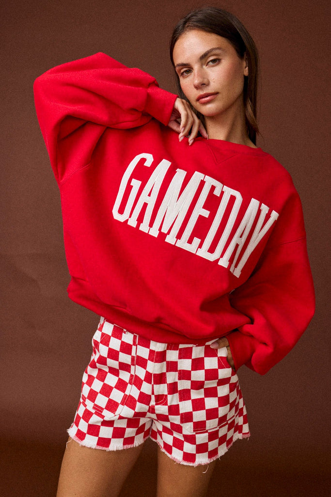 Person wearing a red 'GAMEDAY' sweatshirt and red and white checkered shorts on a brown background