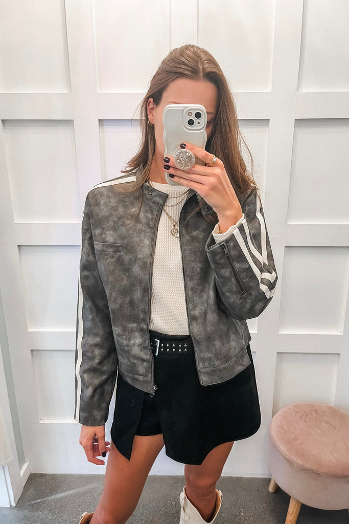 Person taking a mirror selfie wearing a gray jacket with white stripes, white shirt, black shorts, and white sneakers.