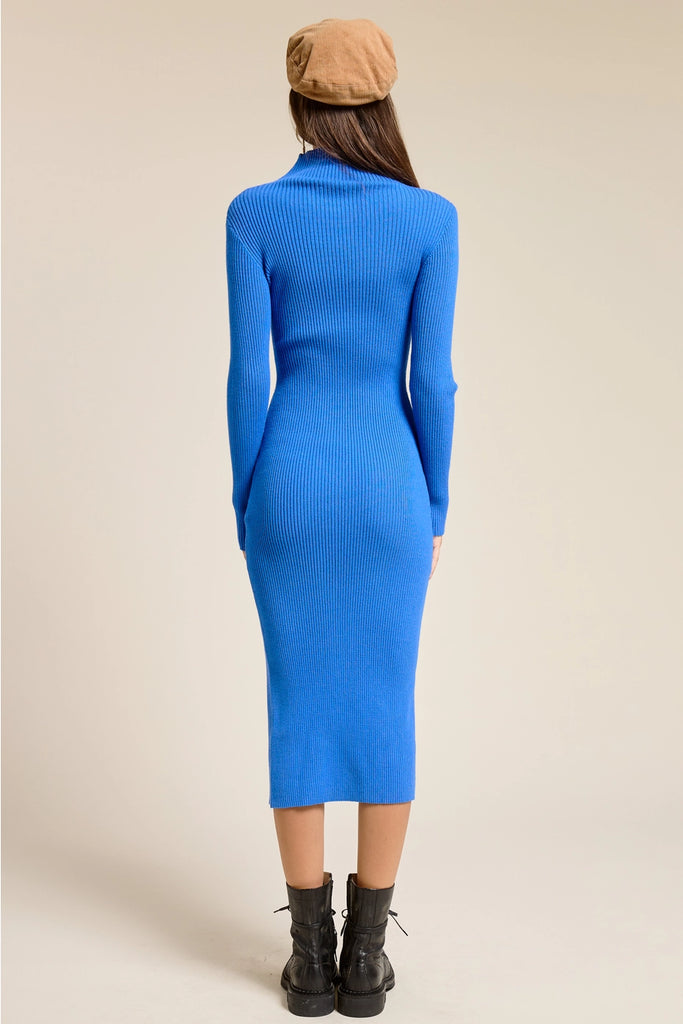 Person wearing a blue ribbed dress with long sleeves and a fitted silhouette on a beige background.