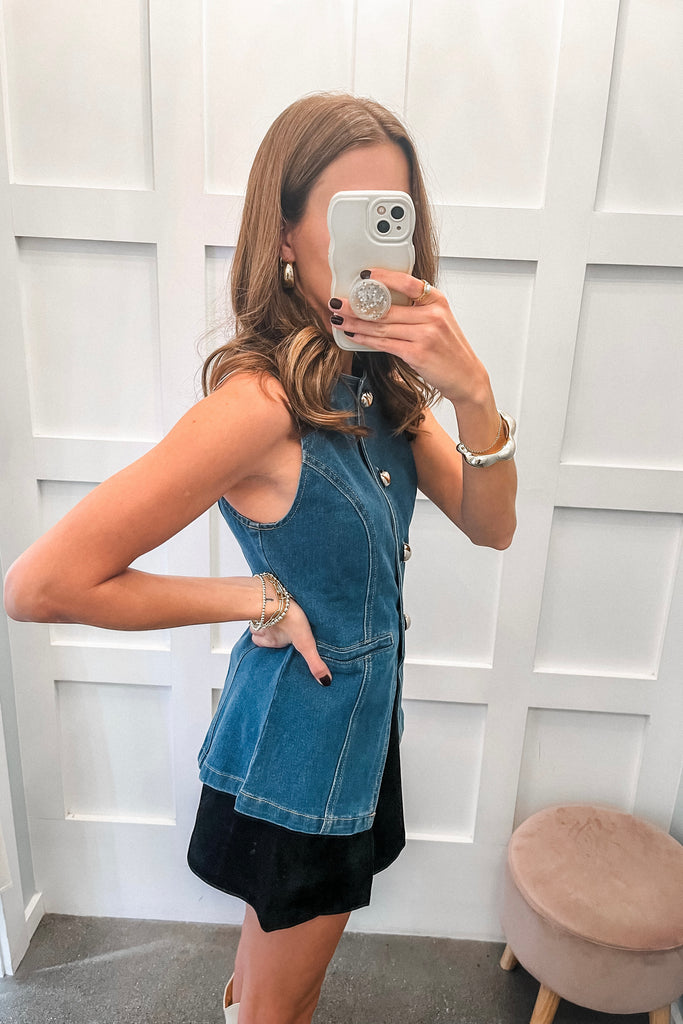 Woman taking a mirror selfie wearing a denim dress with a white wall background