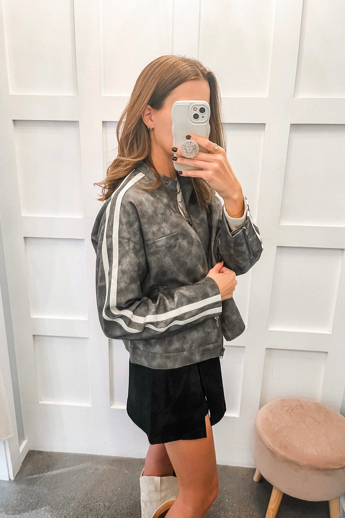 Person wearing a gray sweatshirt with white stripes in a room with a white paneled wall.
