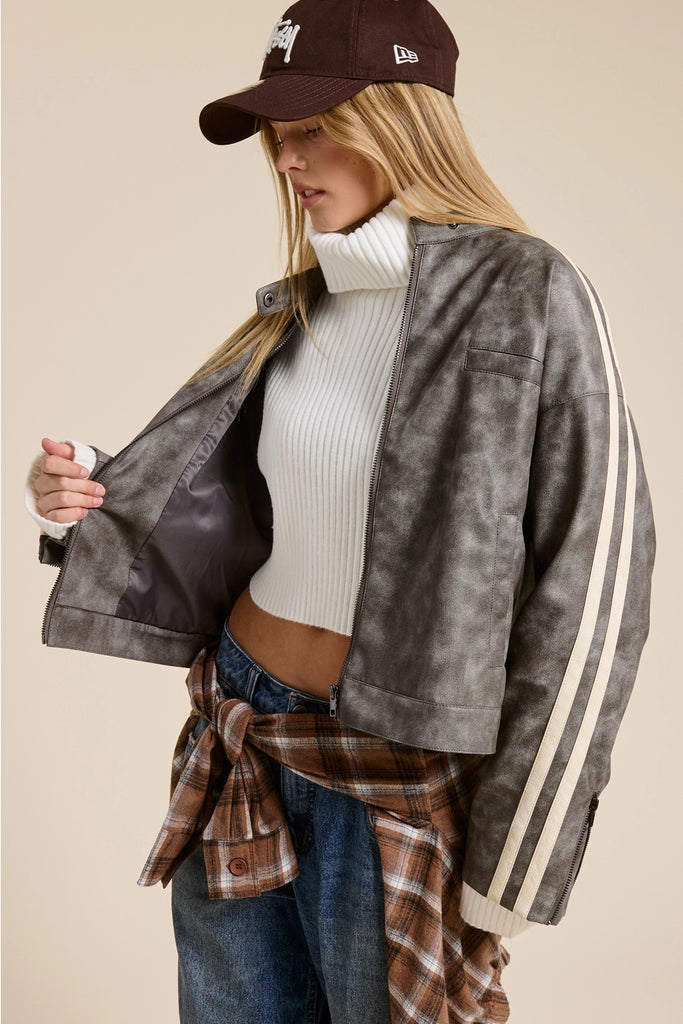 Person wearing a gray jacket with white stripes, white turtleneck, plaid shirt, and jeans on a beige background