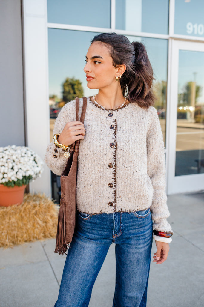 Woman wearing a beige cardigan and blue jeans standing outdoors.