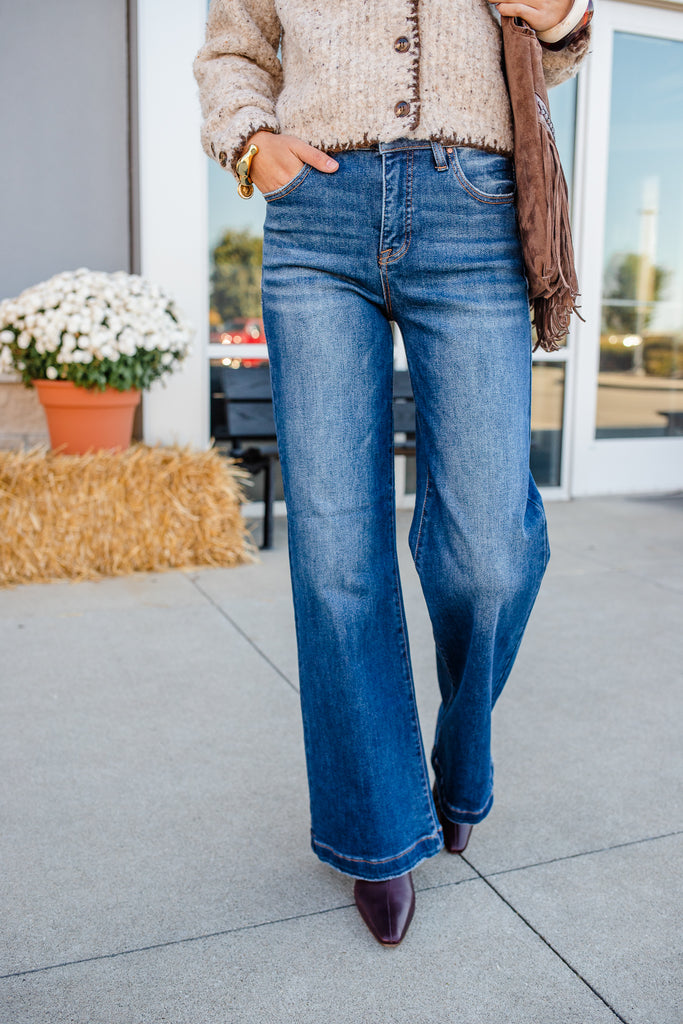 Person wearing blue jeans and a beige cardigan standing outdoors.
