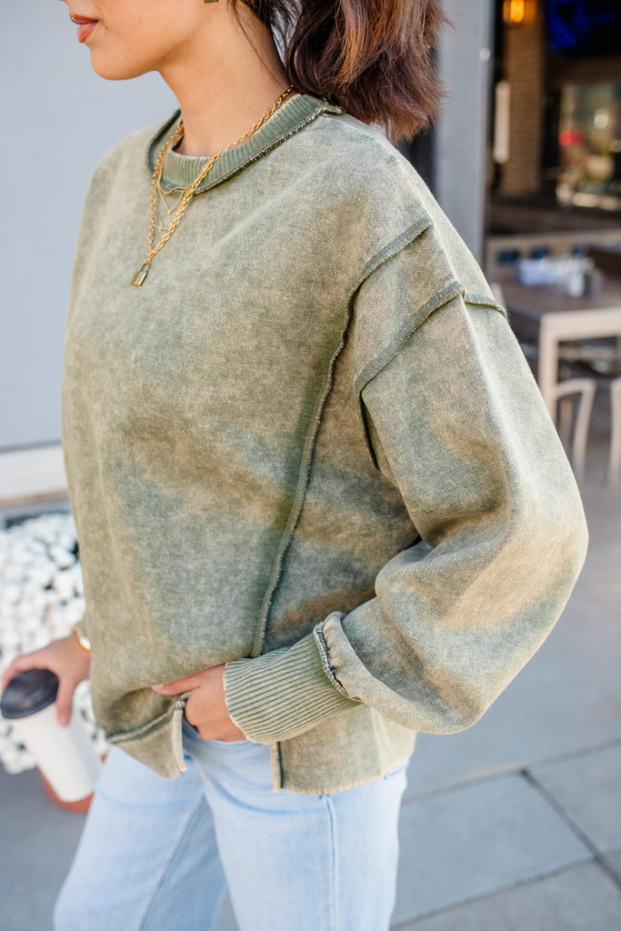 Person wearing a green sweater and light blue jeans outdoors.