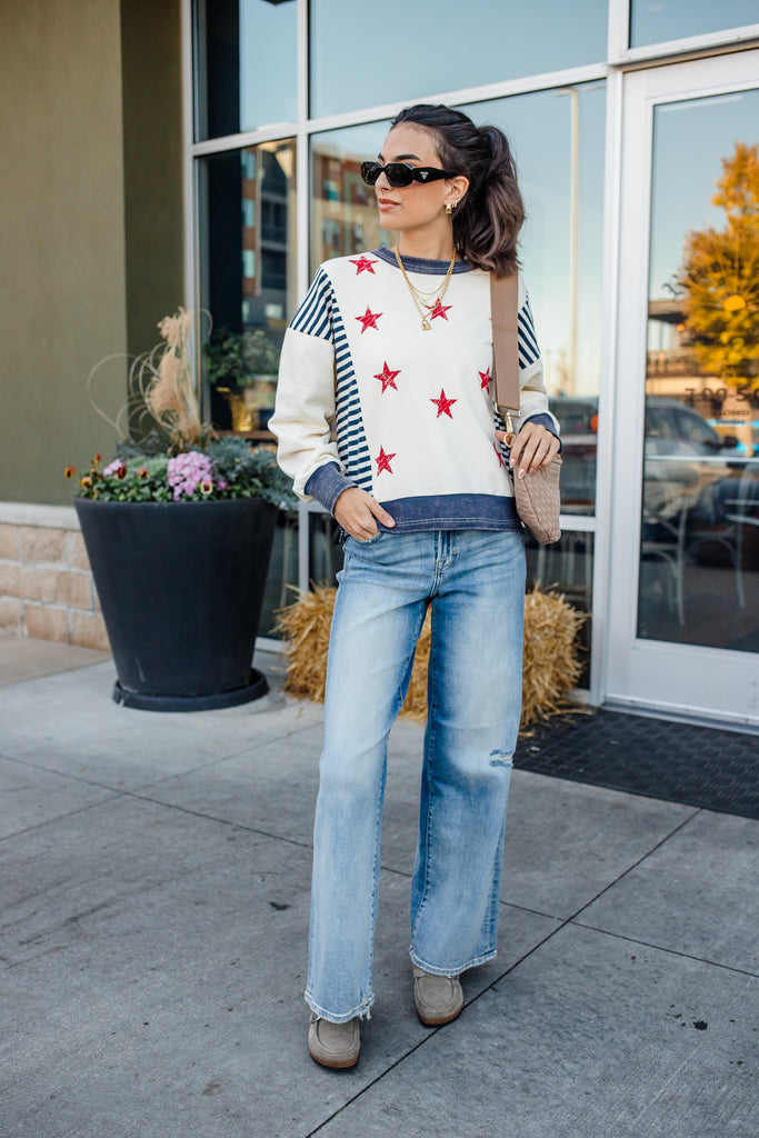 Woman wearing a star-patterned sweater and jeans standing on a sidewalk.