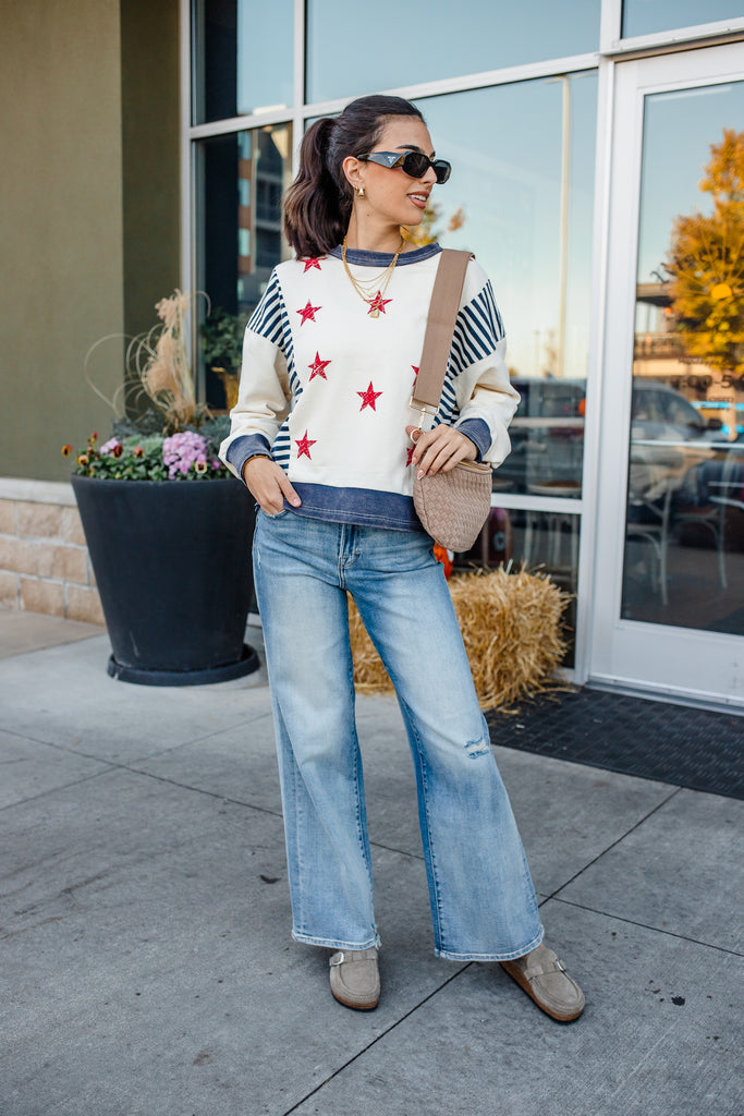 Woman wearing a sweater with star patterns, jeans, and sunglasses outdoors.