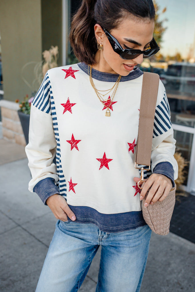 Woman wearing a sweater with red star patterns, blue jeans, and sunglasses outdoors.