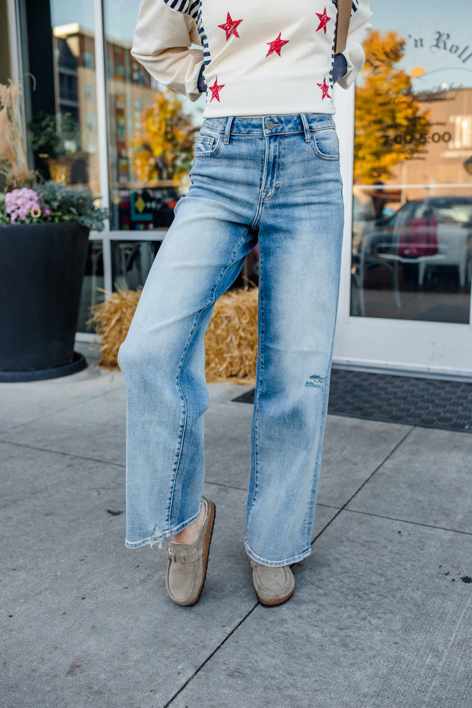 Person wearing a sweater with red star patterns and light blue jeans on a sidewalk.
