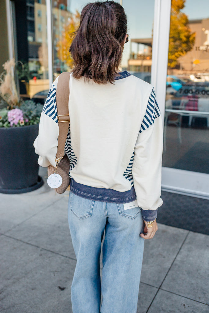 Person wearing a white and blue striped sweater with jeans, standing on a sidewalk.