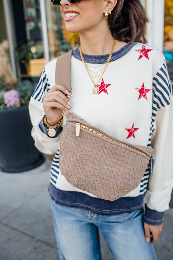 Woman wearing a sweater with red star patterns, holding a brown bag, and smiling outdoors.