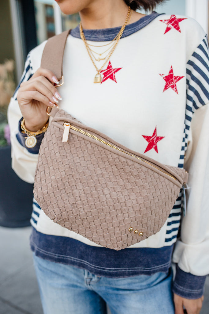 Person wearing a sweater with red star patterns and holding a woven beige bag.