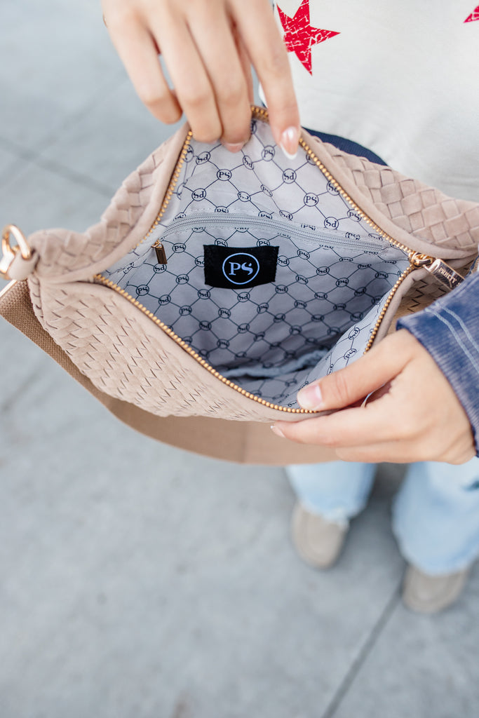 Close-up of a beige handbag with a brand logo, held by a person.