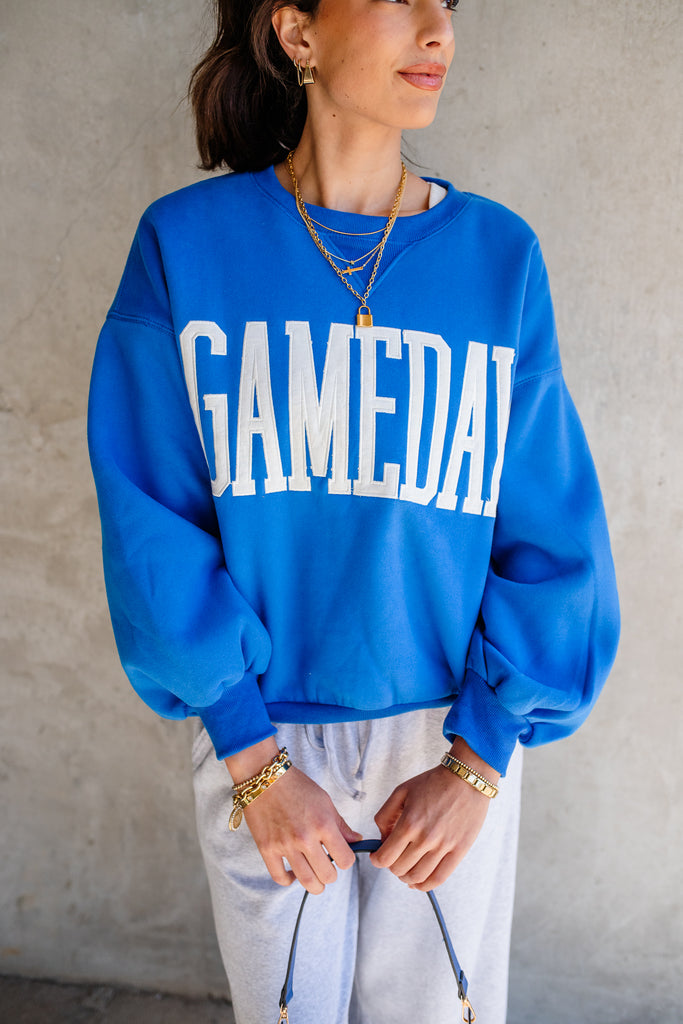 Person wearing a blue 'GAMEDAY' sweatshirt against a plain background