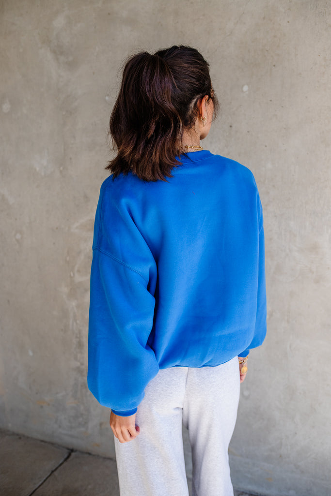 Person wearing a blue sweater and white pants against a gray wall