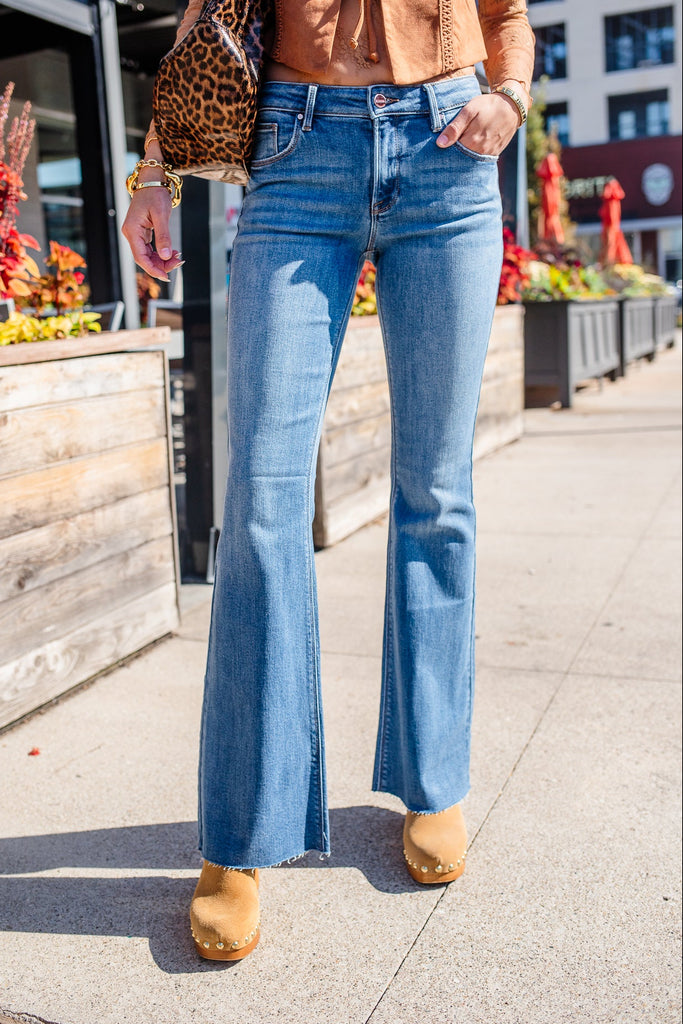 Person wearing blue flared jeans and a brown top on a city street.