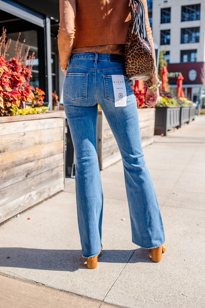 Person wearing blue jeans with a store tag, standing on a sidewalk with plants and buildings in the background.