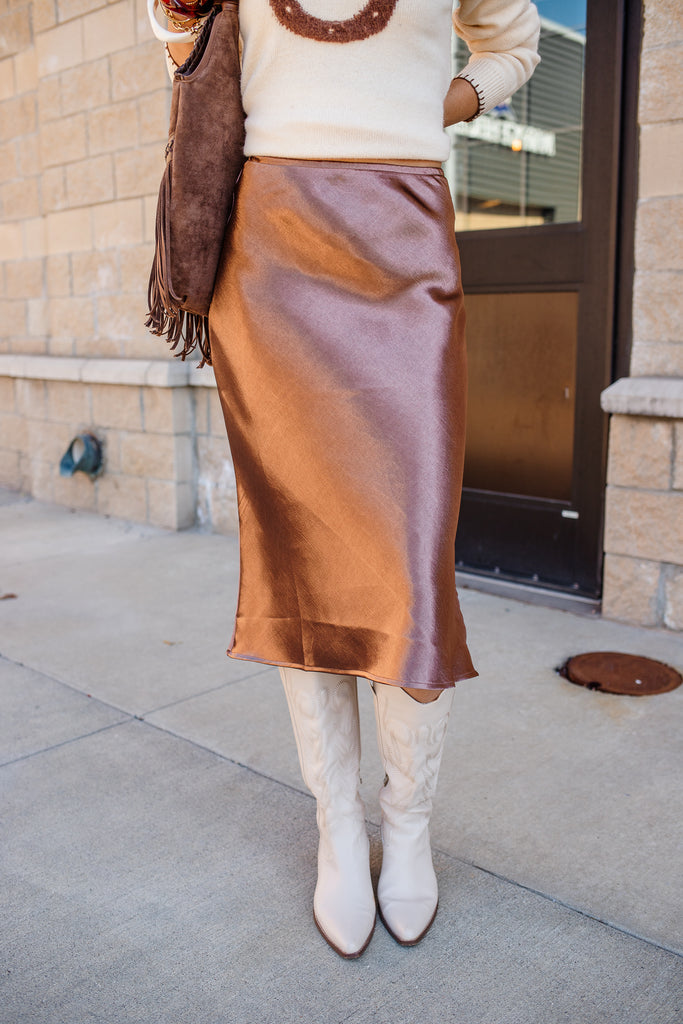Person wearing a brown skirt and white boots on a sidewalk.