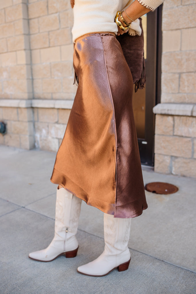Person wearing a brown leather skirt with white boots on a sidewalk.