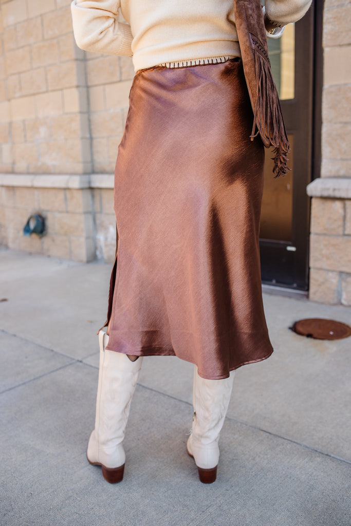 Person wearing a brown skirt and white boots on a sidewalk.