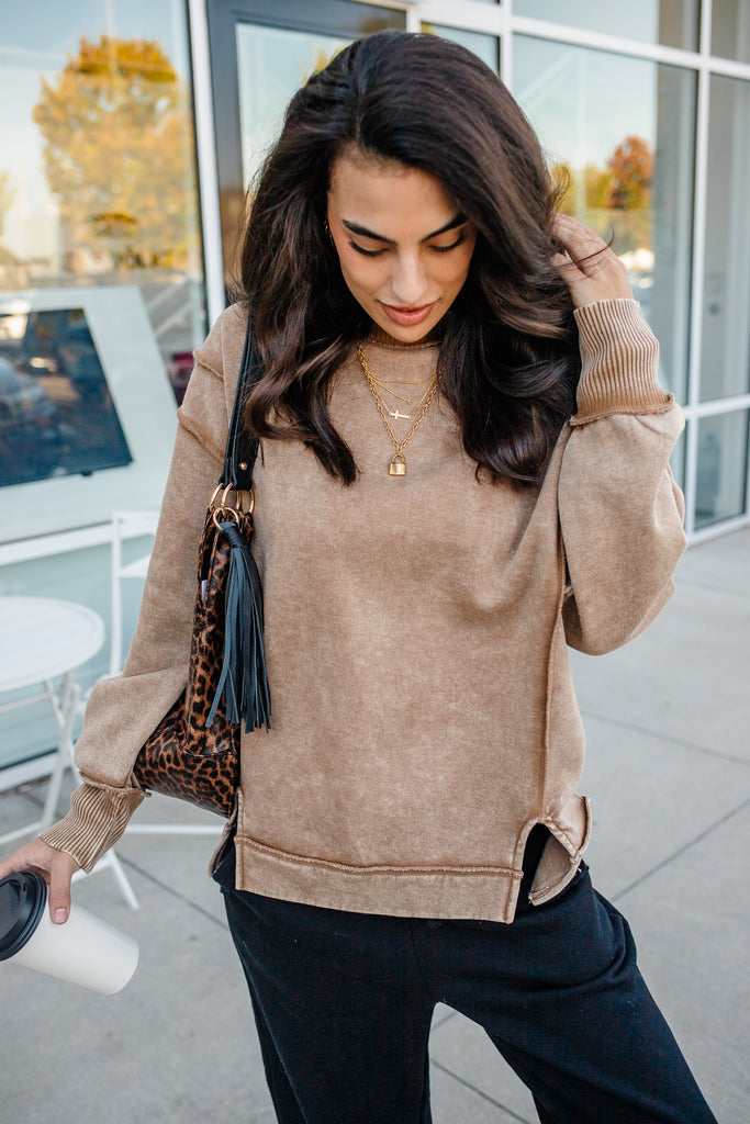 Woman wearing a beige sweater with leopard print sleeves, standing outdoors.