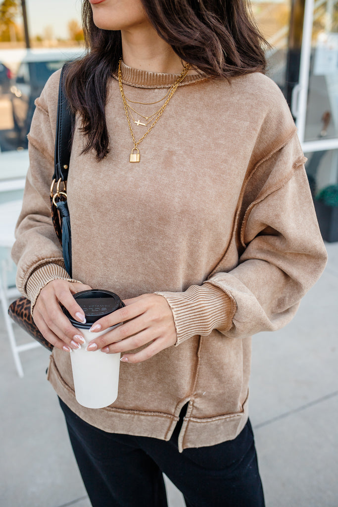 Person wearing a beige sweater holding a coffee cup outdoors