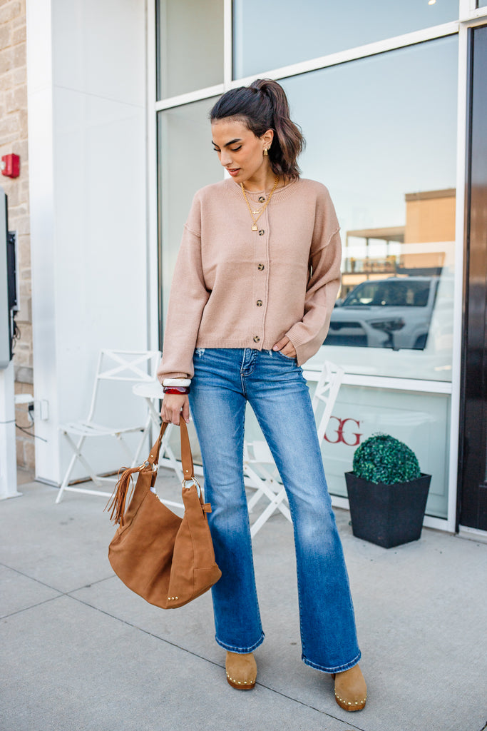 Woman in a beige cardigan and blue jeans standing outside a building.
