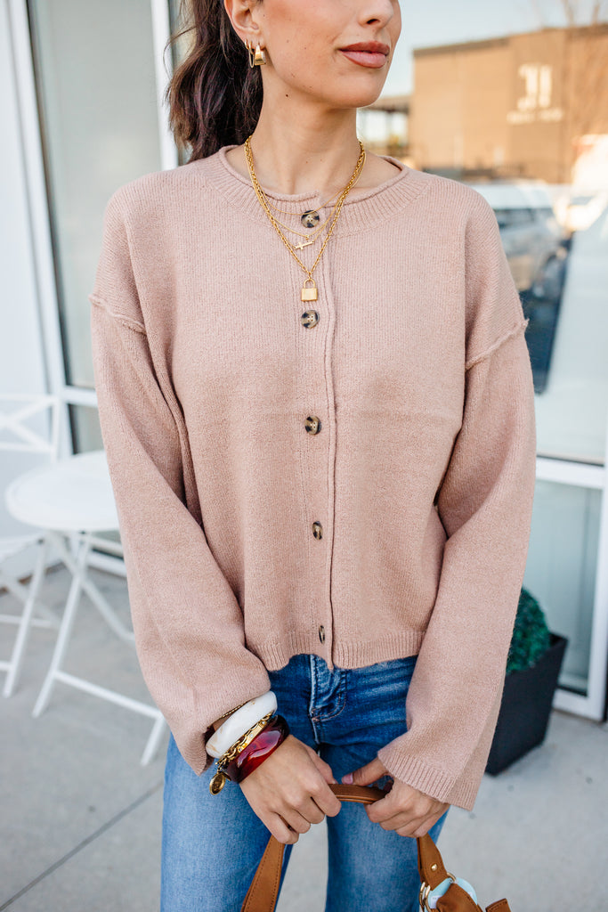 Woman wearing a beige cardigan and blue jeans outdoors