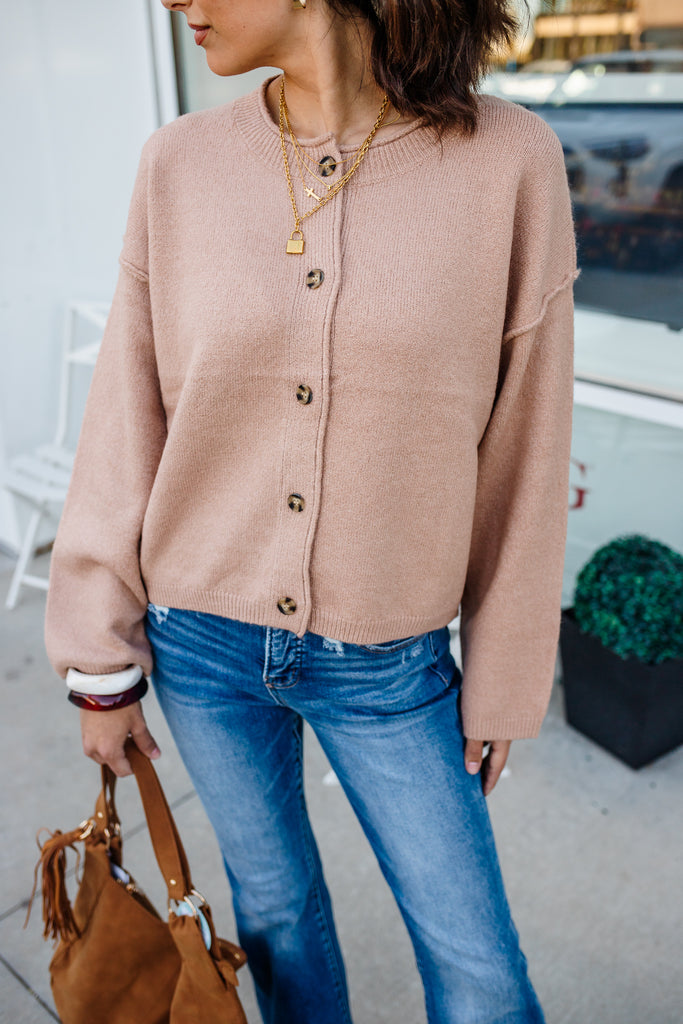 Person wearing a beige cardigan and blue jeans, holding a brown handbag.