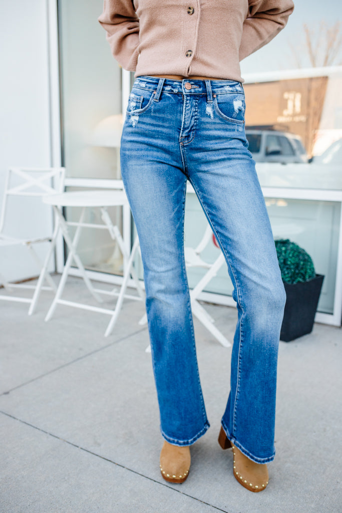 Person wearing blue jeans and a beige cardigan standing on a patio.