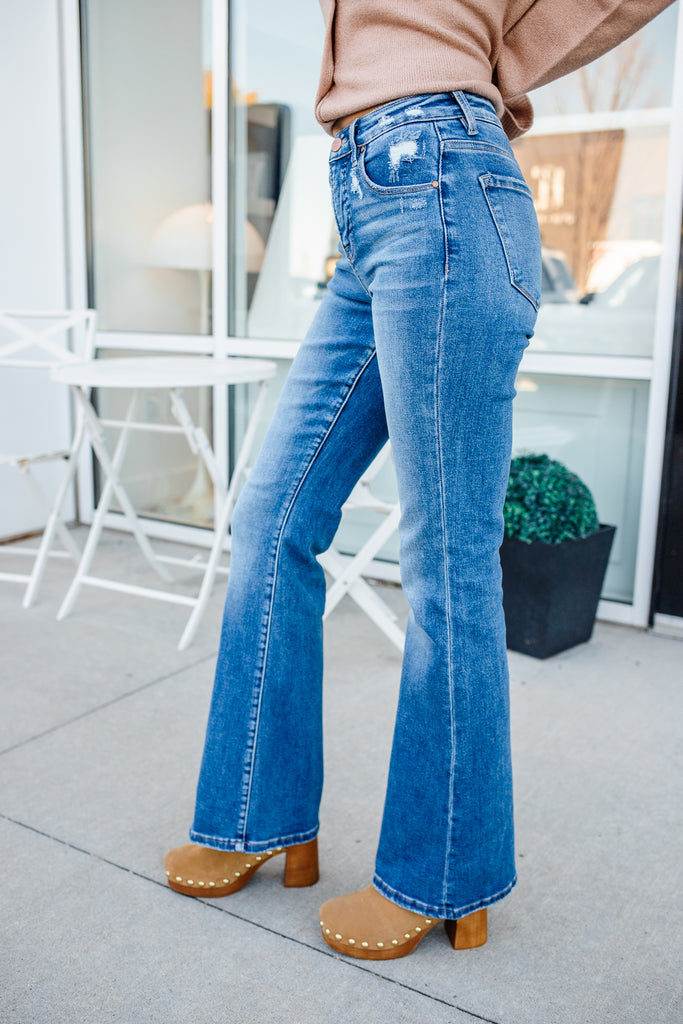 Person wearing blue jeans and brown shoes on a sidewalk.
