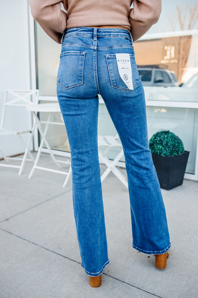 Person wearing blue jeans with a visible brand label, standing on a sidewalk.