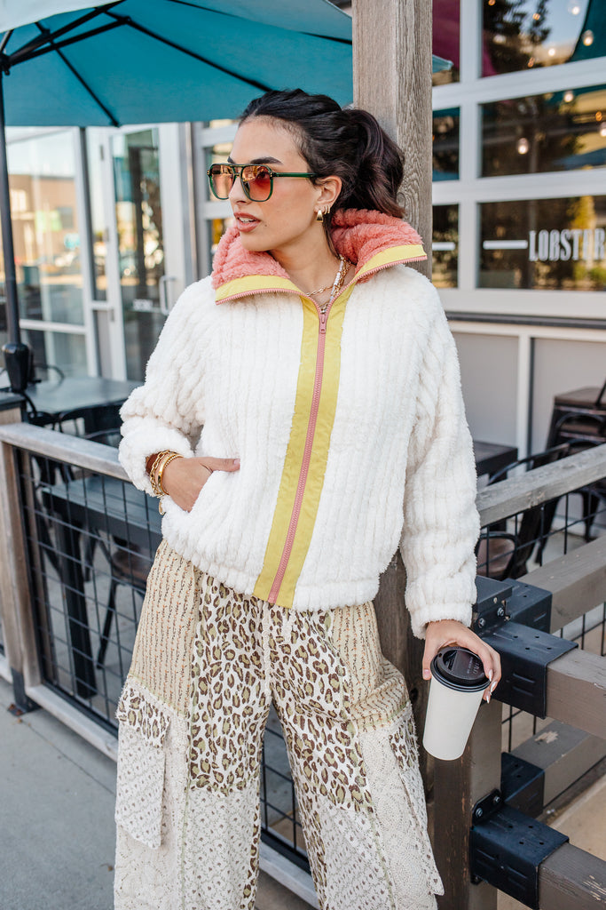 Woman in a stylish outfit with a colorful jacket and leopard print pants, holding a coffee cup.