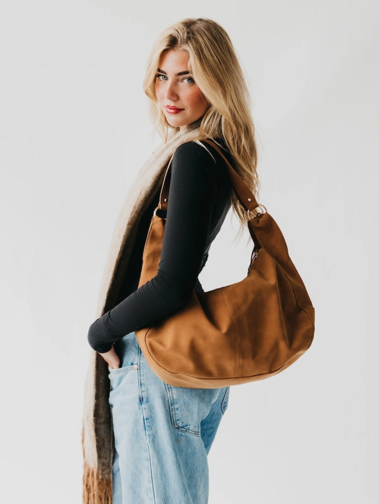 Woman carrying a brown leather handbag against a plain background