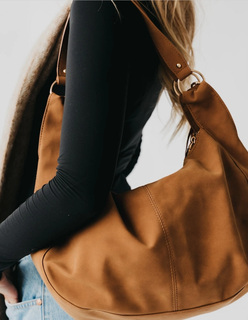 Brown leather handbag being carried by a person wearing a black long-sleeve top.