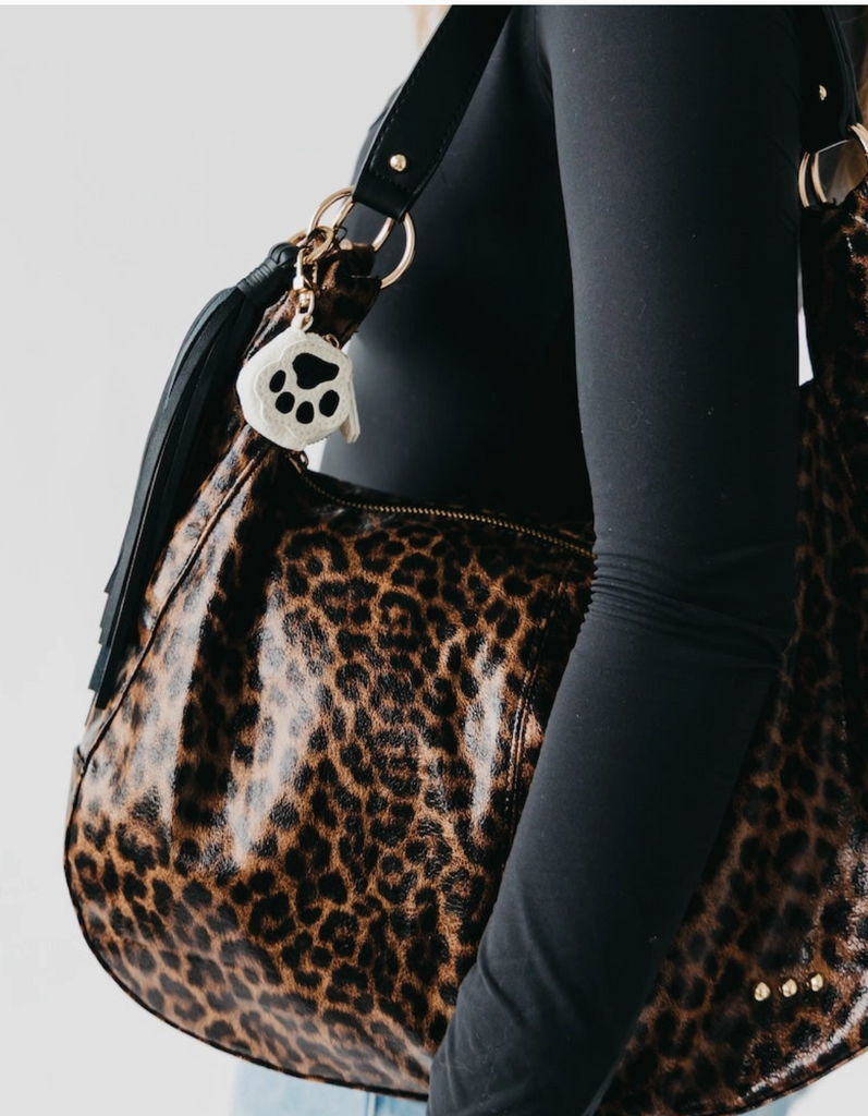 Leopard print handbag with a paw charm held by a person wearing black leggings.