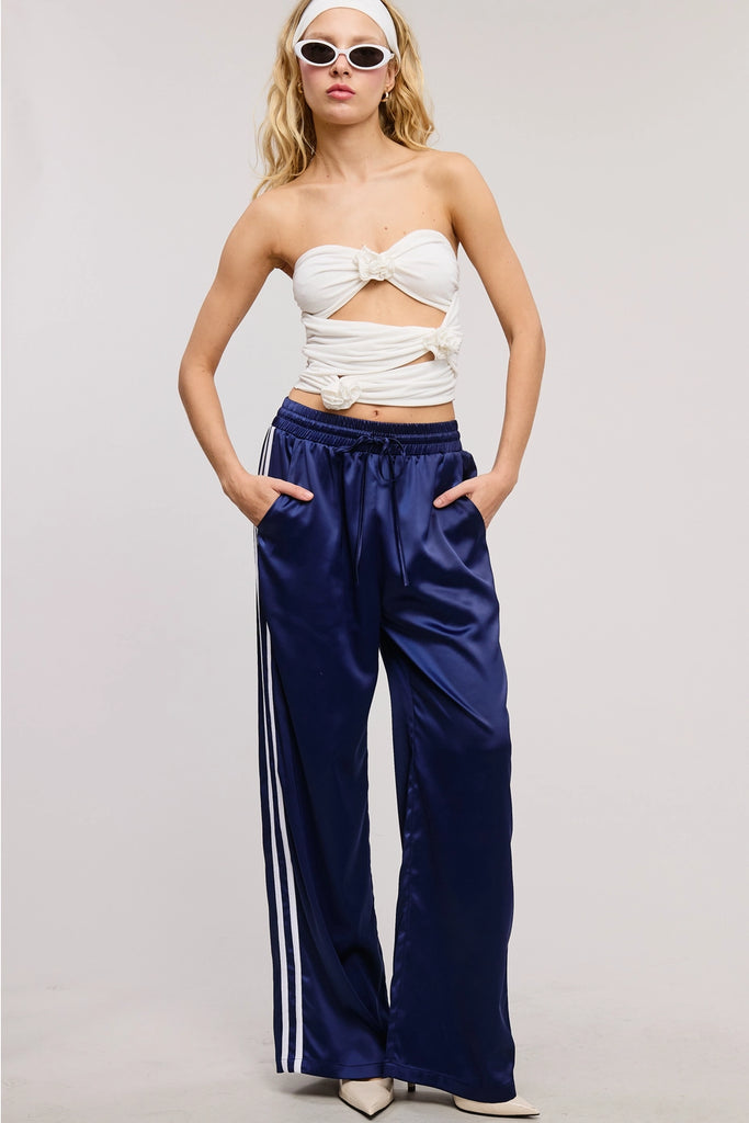 Woman wearing a white strapless top and blue pants with white stripes on a plain background