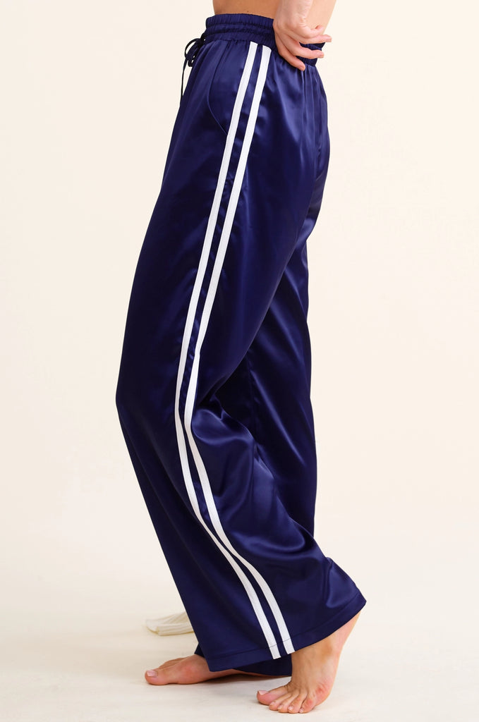 Navy blue track pants with white stripes on a beige background