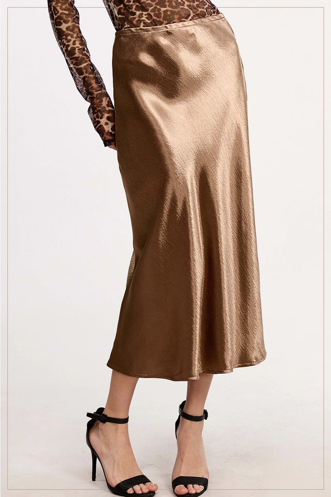 Gold satin skirt worn with leopard print top and black high-heeled sandals on a white background