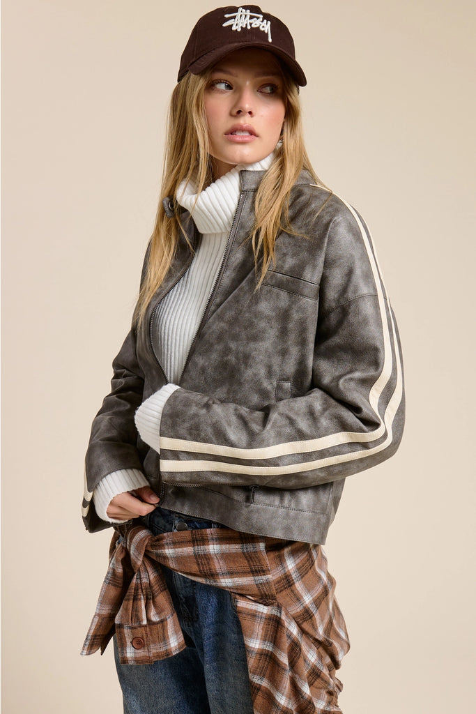 Person wearing a gray jacket with white stripes, plaid shirt, and brown cap on a beige background