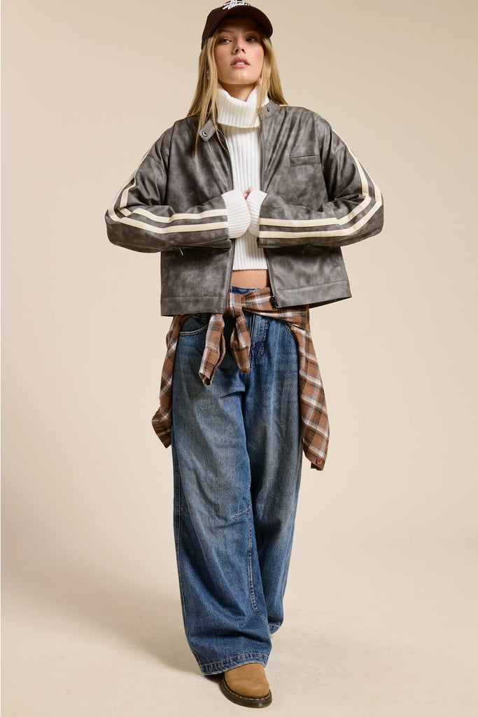 Person wearing a gray jacket with white stripes, plaid shirt, and blue jeans on a beige background