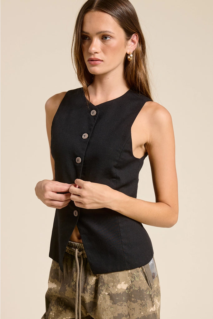 Woman wearing a black sleeveless top with buttons on a beige background