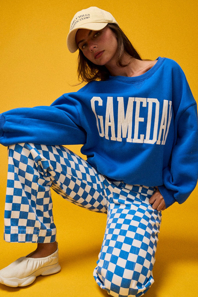 Person wearing a blue 'GAMEDAY' sweatshirt with checkered pants on a yellow background